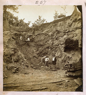 Photograph shows two white men overseeing African American men hammering boulders as others walk with wheelbarrows in a shallow pit phosphate mine, Dunnellon, Florida, 1890. (Library of Congress via AP)