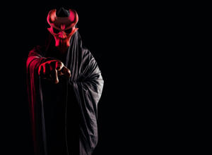 Scary horror occult sectarian priest in black hood and metal mask on black background with red glow. (Getty Images)