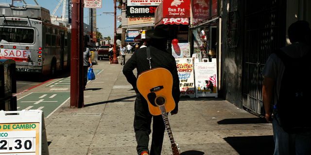 A man carrying a guitar looks for a place to play music in the Mission District in San Francisco.