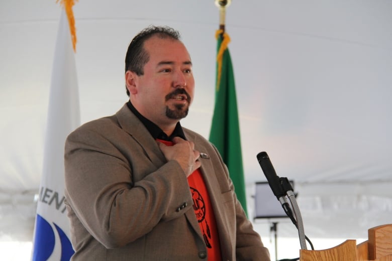 A leader in a blazer and orange shirt speaks into a microphone.